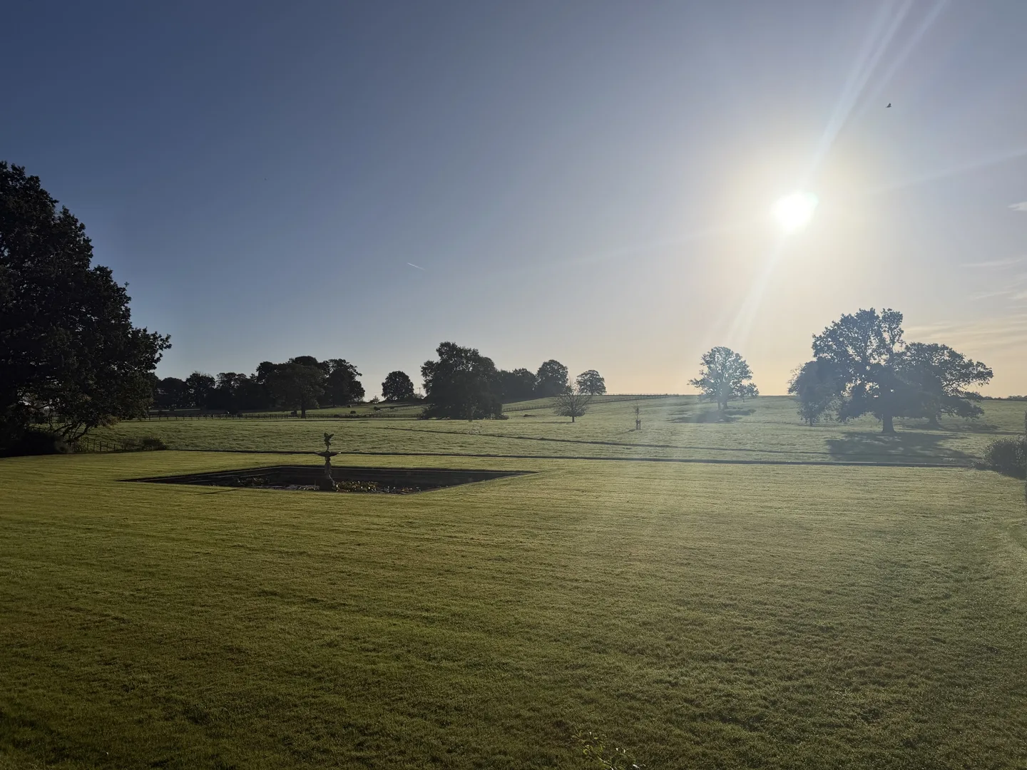 Morning sun over the lawn, garden fountain and parkland trees